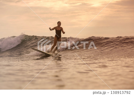 Athletic Female Surfer Displaying Power And Poise On Sunset Ocean Wave Athletic Female Surfer Displaying Power And Poise On Sunset Ocean Wave 138913792