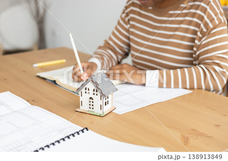 female architect designer is working, taking notes in notebook is mock up of house on table. 138913849