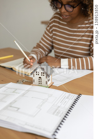 female architect designer is working, taking notes in notebook is mock up of house on table. 138913850