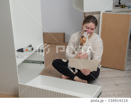A Caucasian woman assembles furniture with her cute dog. A Caucasian woman assembles furniture with her cute dog. 138914218