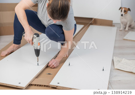 A Caucasian woman uses a screwdriver to tighten a screw while assembling a cabinet. 138914219