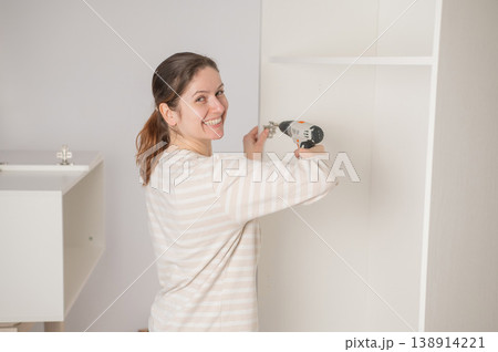 A Caucasian woman uses a screwdriver to tighten a screw while assembling a cabinet. 138914221