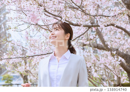 満開の桜の下で微笑むスーツ姿の若い女性・春の新生活イメージ・新入社員の入社式シーズン 138914740
