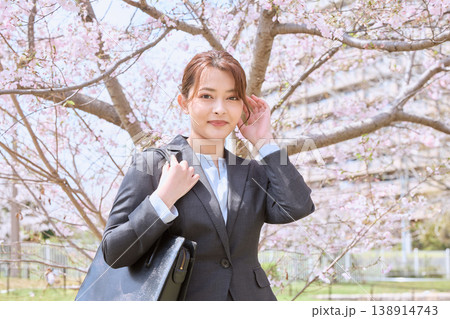 桜の下でポーズをとるリクルートスーツ姿の若い女性・春の新生活イメージ・就職活動中の女子大学生 138914743