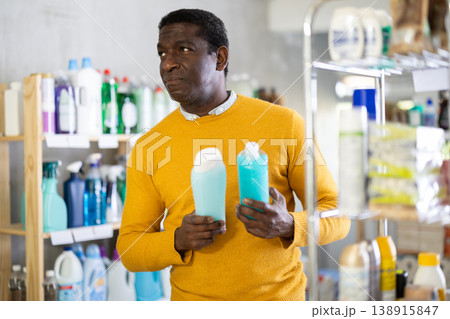 Male buyer chooses shampoo or shower gel in household goods department of supermarket 138915847