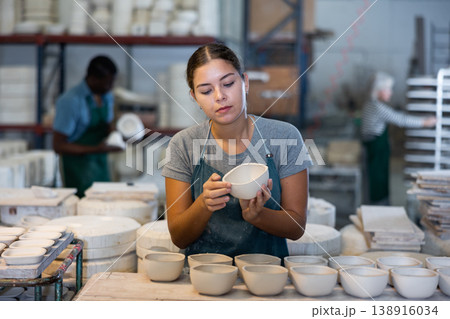 Young woman checks quality of pottery after being removed from plaster mold Young woman checks quality of pottery after being removed from plaster mold 138916034