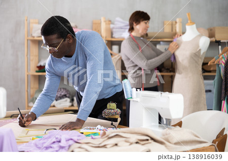 Male fashion designer drafting clothing pattern in studio with female colleague Male fashion designer drafting clothing pattern in studio with female colleague 138916039