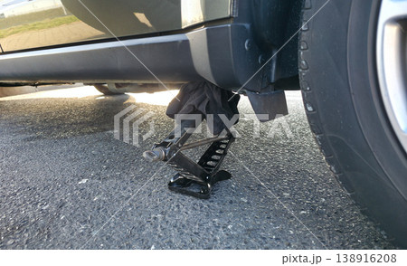 A hand-held portable jack is installed under a car to lift the vehicle for changing a tire. High quality photo A hand-held portable jack is installed under a car to lift the vehicle for changing a tire. High quality photo 138916208