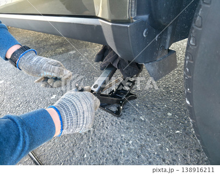 A young man lifts a car with a hand jack to replace a damaged tire with a spare one. High quality photo A young man lifts a car with a hand jack to replace a damaged tire with a spare one. High quality photo 138916211