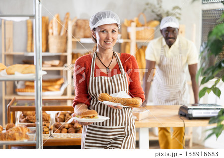 Woman entrepreneur, owner of bakery, holds out sandwich in disposable dish plate in hand Woman entrepreneur, owner of bakery, holds out sandwich in disposable dish plate in hand 138916683