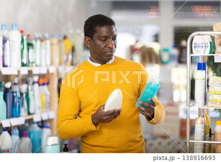 Male buyer chooses shampoo or shower gel in household goods department of supermarket Male buyer chooses shampoo or shower gel in household goods department of supermarket 138916693