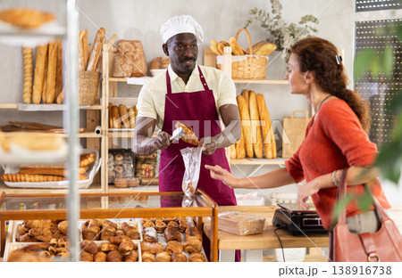 Man baker packaging croissants in a plastic bag for customer 138916738