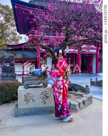 神社の梅の木の下で牛の像を撫でる着物の人 神社の梅の木の下で牛の像を撫でる着物の人 138919740