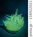 A close up view of sharp, translucent green crystals forming in a glass petri dish under blue light, showcasing natural geometric growth patterns 138922021