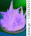 Close up view of sharp, translucent crystals forming in a petri dish under purple and green lighting, showcasing a scientific experiment 138922023