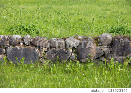 A low rustic stone wall covered in moss sits amid a vibrant green meadow 138923545