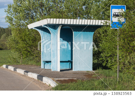 A weathered blue bus stop shelter sits empty beside a quiet country road 138923563