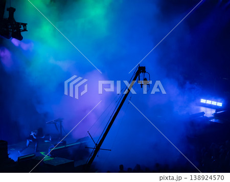 Dynamic concert stage with performer silhouette, dramatic blue and green smoke, and a camera crane capturing the electrifying live music production Dynamic concert stage with performer silhouette, dramatic blue and green smoke, and a camera crane capturing the electrifying live music production 138924570