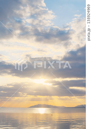 夕暮れ時の静かな湖面と遠くの山並み、空に浮かぶ雲 夕暮れ時の静かな湖面と遠くの山並み、空に浮かぶ雲 138924969