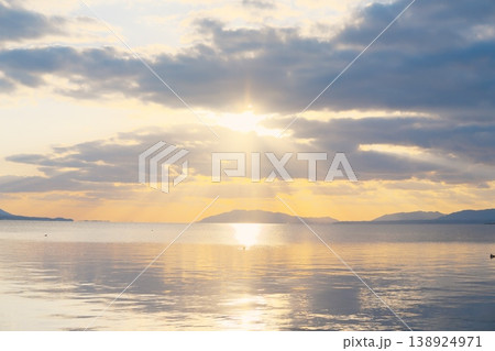 夕暮れ時の静かな湖面と遠くの山並み、空に浮かぶ雲 夕暮れ時の静かな湖面と遠くの山並み、空に浮かぶ雲 138924971
