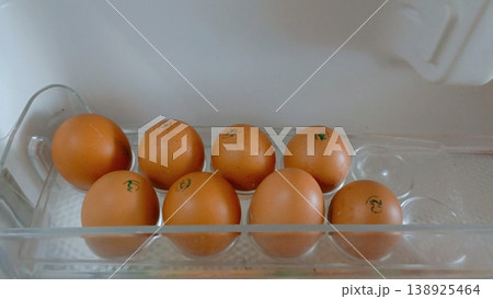 Eight brown chicken eggs with blue quality stamps arranged in a clear plastic refrigerator door shelf. Eight brown chicken eggs with blue quality stamps arranged in a clear plastic refrigerator door shelf. 138925464