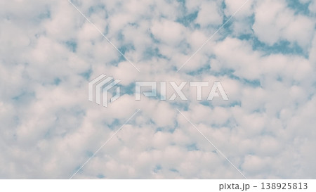 A wide view of small, fluffy white altocumulus clouds densely covering a bright blue sky, creating a soft natural pattern 138925813