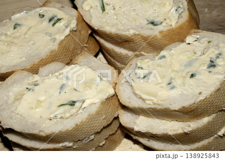 Fresh cut baguette bread in slices with herb garlic butter on a wooden background Fresh cut baguette bread in slices with herb garlic butter on a wooden background 138925843