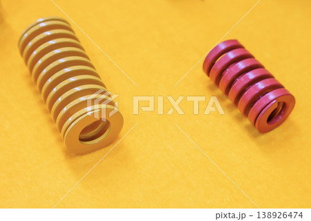 Group of yellow and red industrial compression die springs on a matching yellow background. 138926474