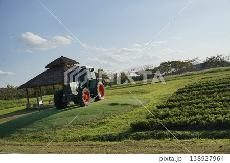 Tractor is driving down a field with a green hill in the background Tractor is driving down a field with a green hill in the background 138927964