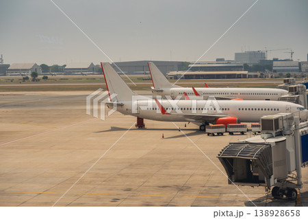 Three Commercial Airplanes Parked at a Modern Airport Terminal Under Clear Sky with Industrial Buildings in Background 138928658