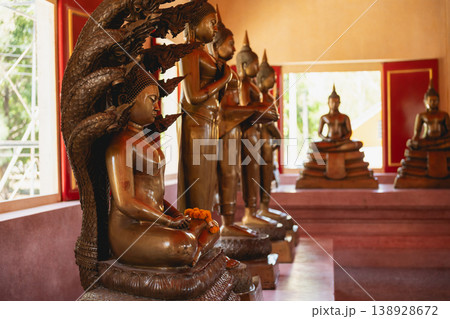 Serene Buddhist Temple Interior with Statues of Golden Buddha Surrounded by Intricate Sculptures and Natural Light Illuminating Sacred Space Serene Buddhist Temple Interior with Statues of Golden Buddha Surrounded by Intricate Sculptures and Natural Light Illuminating Sacred Space 138928672