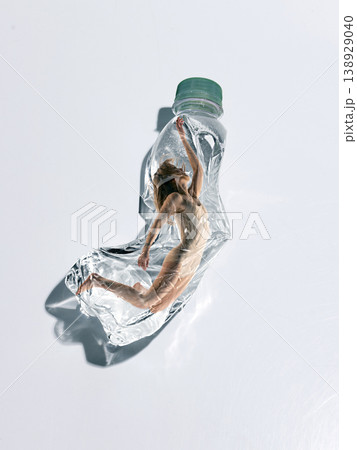 Woman stretching inside crushed plastic bottle symbolizing fight for freedom and movement. Woman stretching inside crushed plastic bottle symbolizing fight for freedom and movement. 138929040