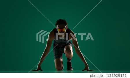 Male athlete in low sprint start position facing camera on green background. 138929121