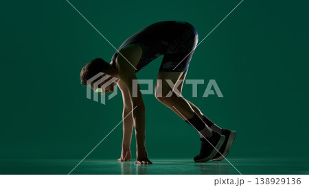Male athlete in sprint start position viewed from side on green studio background Male athlete in sprint start position viewed from side on green studio background 138929136