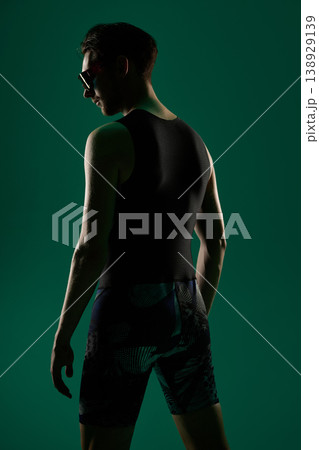 Male athlete standing back view in sportswear on dark green studio background Male athlete standing back view in sportswear on dark green studio background 138929139