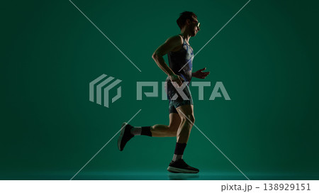 Male athlete captured mid stride running in side view on dark green background Male athlete captured mid stride running in side view on dark green background 138929151