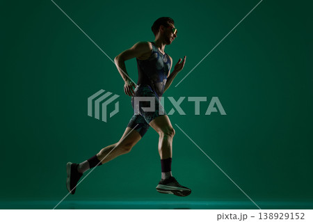 Male athlete running in side view full body motion on dark green background. Male athlete running in side view full body motion on dark green background. 138929152
