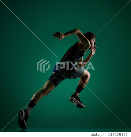 Male athlete accelerating forward in dynamic running pose on dark green. 138929155
