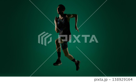 Male athlete captured in vertical jump in motion on dark green background. 138929164