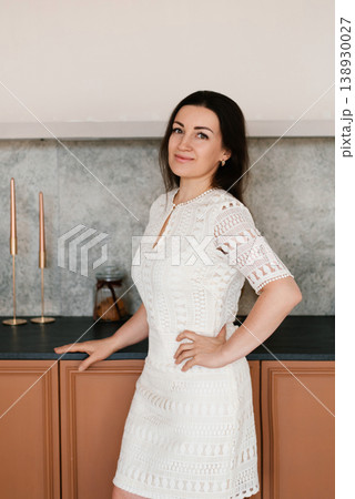 Elegant Lady in White Dress standing near Kitchen Counter Elegant Lady in White Dress standing near Kitchen Counter 138930027