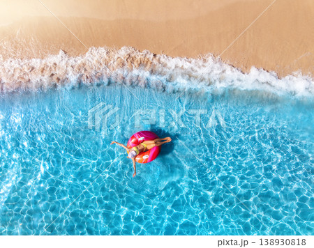 Aerial view of a woman on pink inflatable ring, blue sea, waves Aerial view of a woman on pink inflatable ring, blue sea, waves 138930818