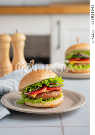 Meat burger with tomato, cheese, and lettuce on a plate on a table with spice and napkin Meat burger with tomato, cheese, and lettuce on a plate on a table with spice and napkin 138931643