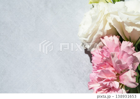 Fresh pink carnations and white eustomas on a light textured background with sunlight, top view. 138931653