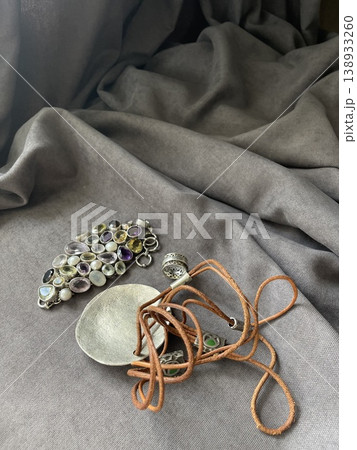 Jewelry items and a silver spoon arranged on gray fabric during daytime 138933260