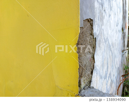 Close-up of damaged exterior concrete wall with peeling yellow paint revealing rough brown plaster, ideal for grunge texture background and renovation themes 138934090