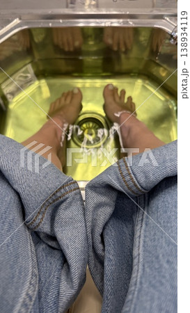 Feet soaking in pedicure spa bath with jeans visible, showcasing relaxation and self-care Feet soaking in pedicure spa bath with jeans visible, showcasing relaxation and self-care 138934119