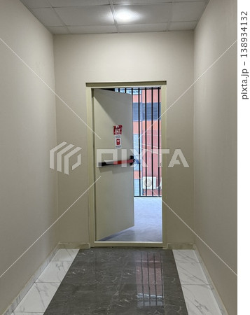 Emergency exit in modern building hallway with marble floor and barred window view in urban setting 138934132