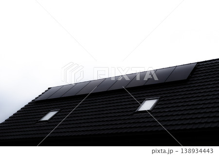 Minimalist view of solar panels on black tiled roof against white sky 138934443