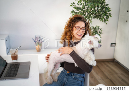 Woman working from home embracing pet dog on lap Woman working from home embracing pet dog on lap 138934515