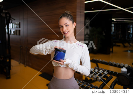 Woman holding protein supplement container enjoying active gym lifestyle 138934534